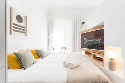 a white bedroom with a large bed with a flat screen tv at GuestReady - Studio Five-0-Five in Porto